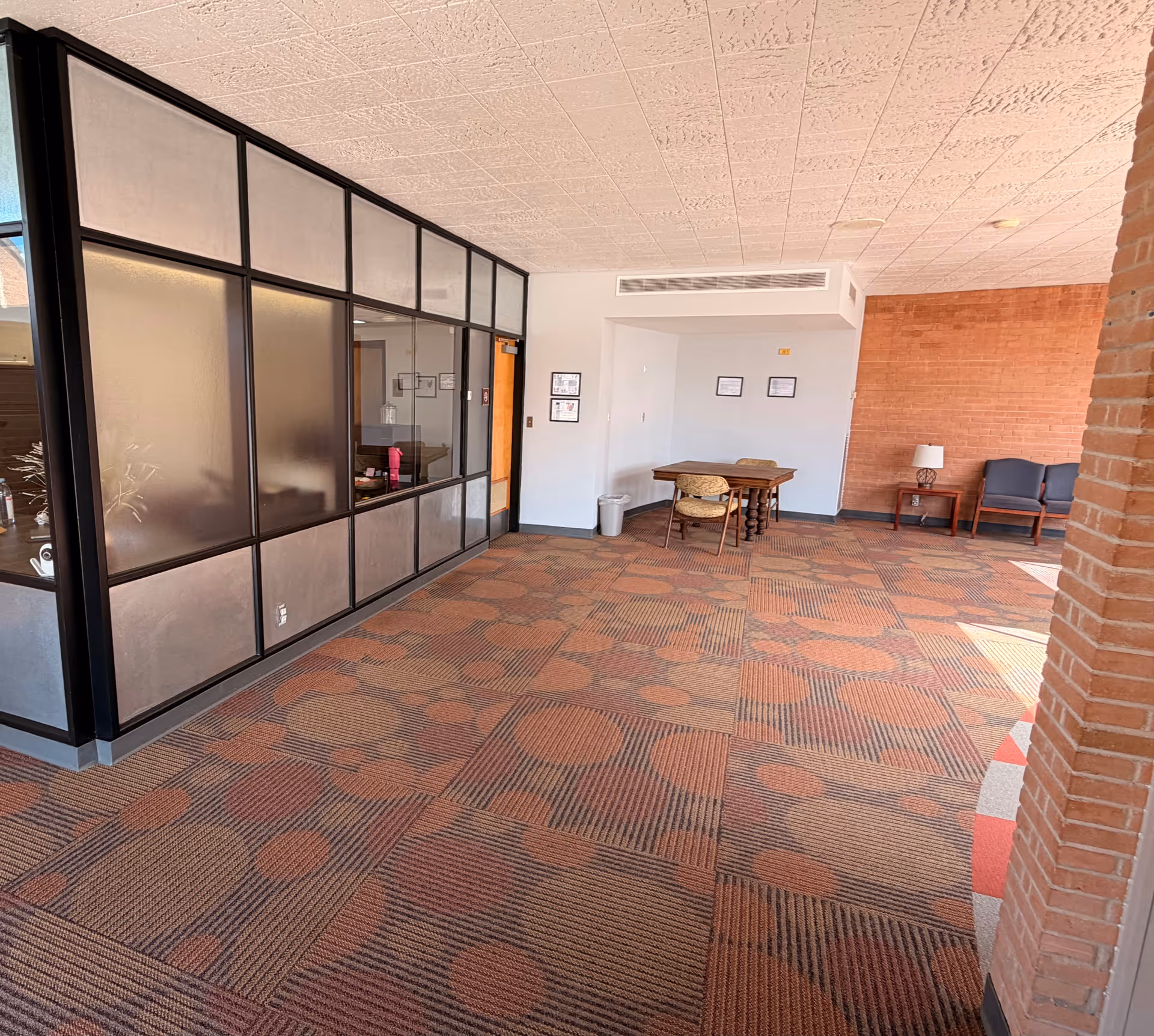 Spacious indoor lobby with frosted glass partition, brick wall, carpeted floor, and seating.