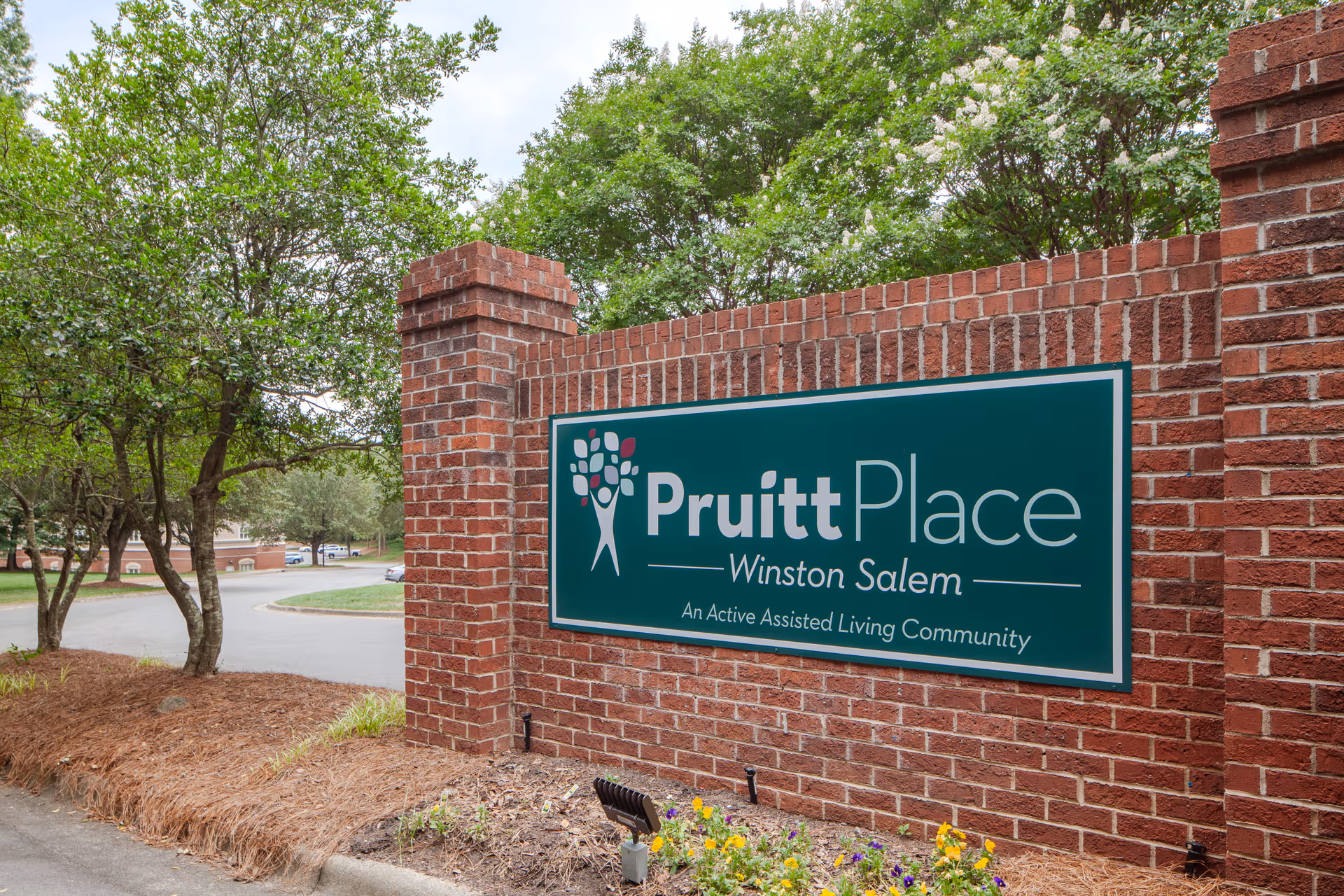 Exterior brick sign reading PruittPlace Winston Salem beside a curved road