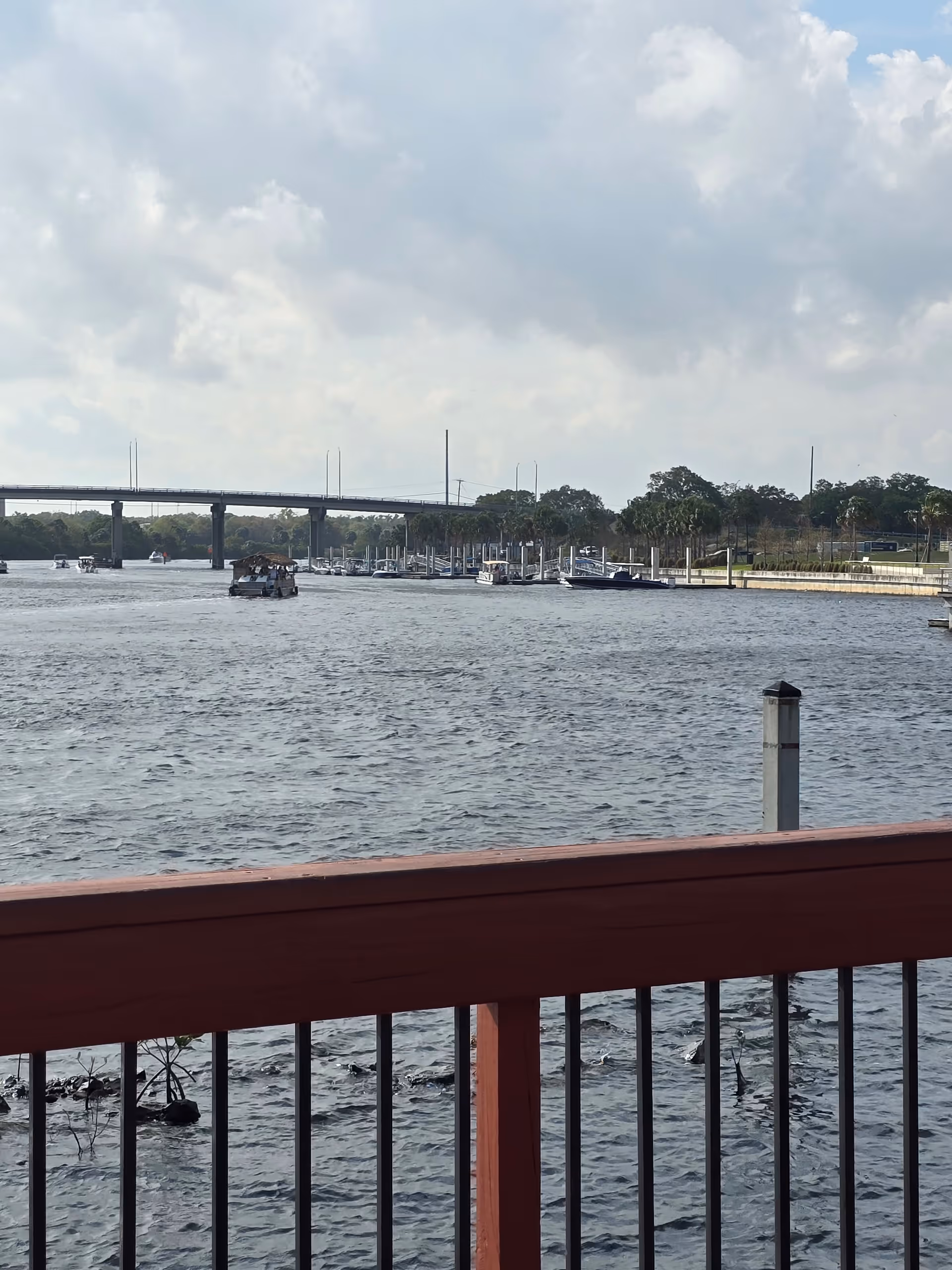 Waterfront view from a deck with a red railing, boats, and a bridge.