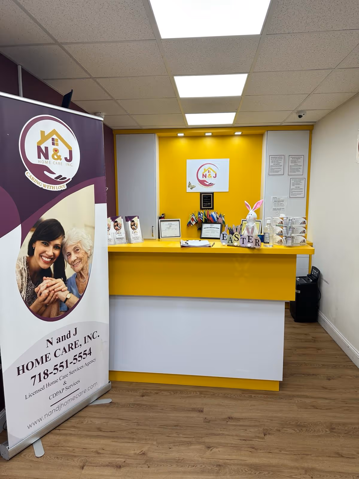 Reception desk with yellow counter inside N and J Home Care facility, banners and certificates.