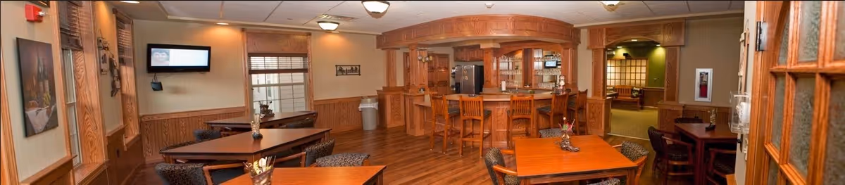 Interior common room with a wood-paneled bar, several dining tables and chairs, and a wall-mounted television.