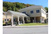 Two-story senior living facility with beige exterior, covered entry, and manicured landscaping.