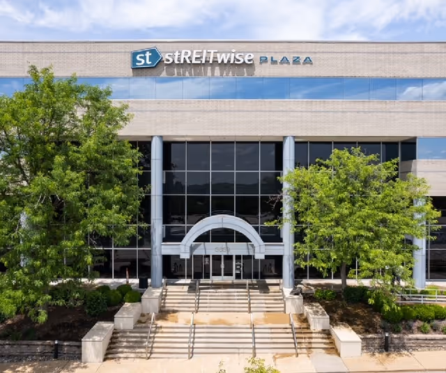 Exterior view of a modern building entrance with glass façade and surrounding trees.