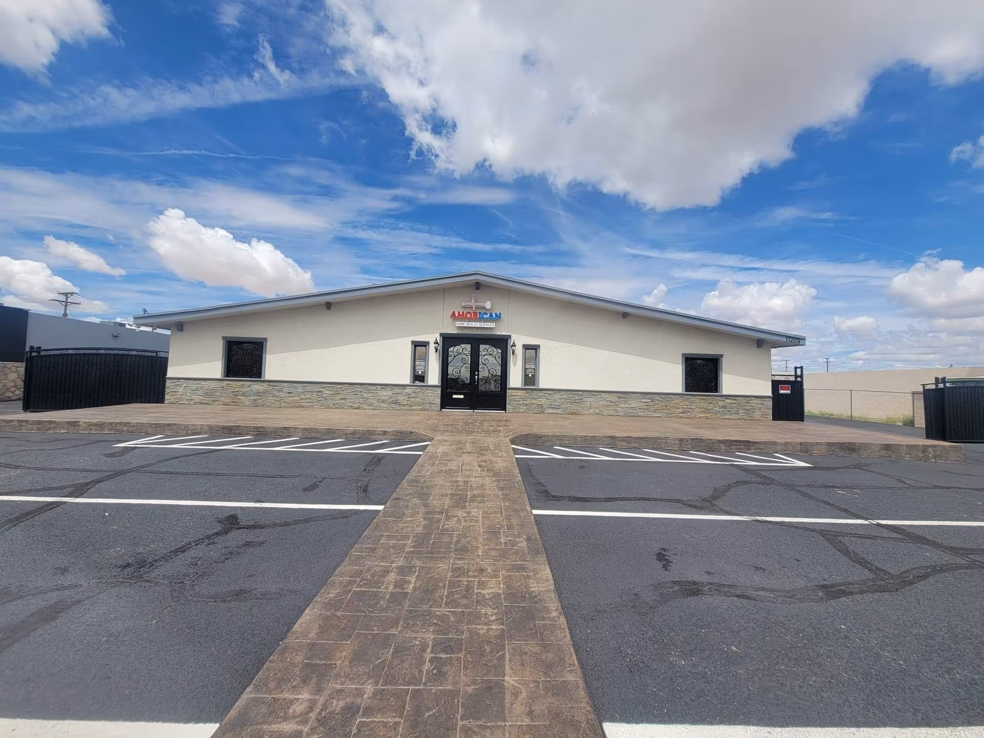 Facility front exterior with entry doors and a paved parking lot under a blue sky.