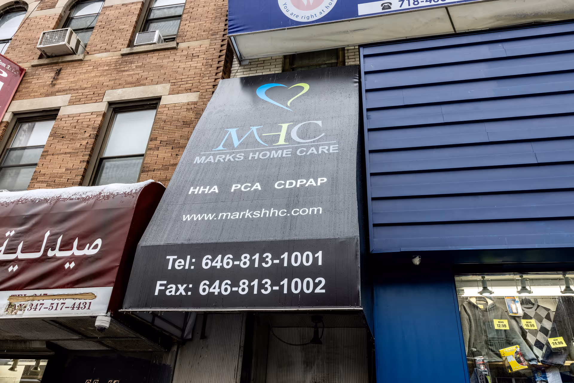 Storefront sign for MHC Marks Home Care with phone numbers on a city street.