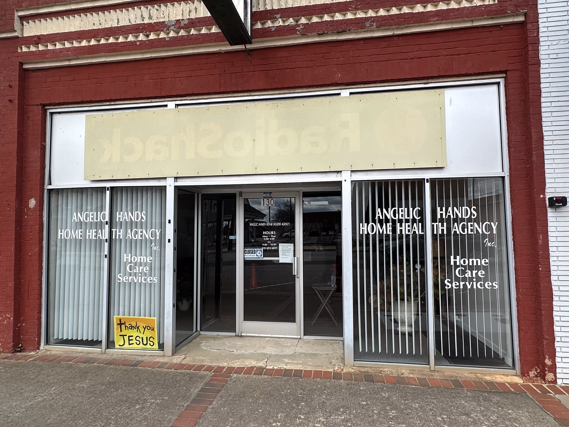 Storefront with glass doors and vertical blinds displaying Angelic Hands Home Health Agency signage.