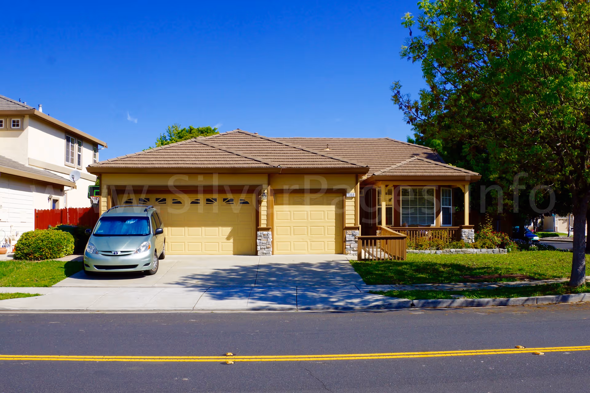 A beige single-story house with a two-car garage and a parked silver sedan.