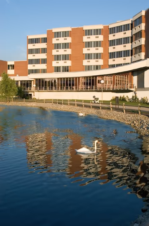 Brick retirement facility overlooking a pond with a swan gliding on the water.