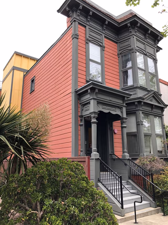Exterior view of a red and gray Victorian-style building with a front porch and stairs.