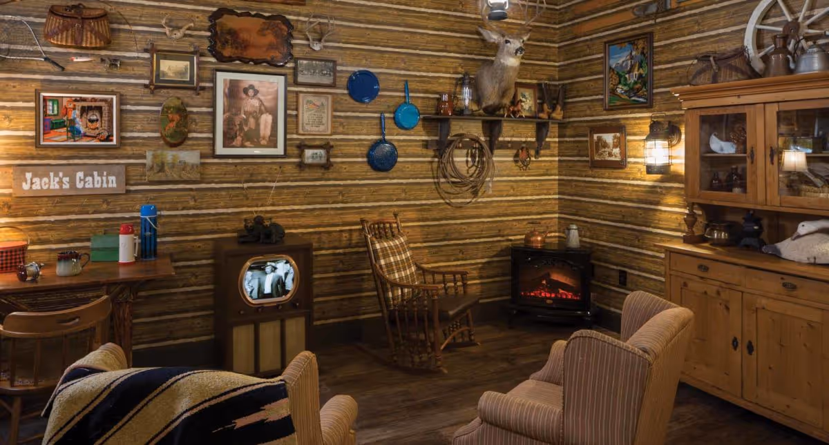 Cozy cabin-style living room with wood-paneled walls, vintage TV, rocking chair, fireplace, and rustic decor.