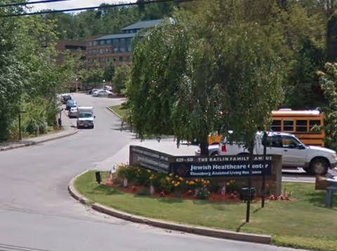 Exterior view of the facility entrance with a sign and surrounding trees on a curving road