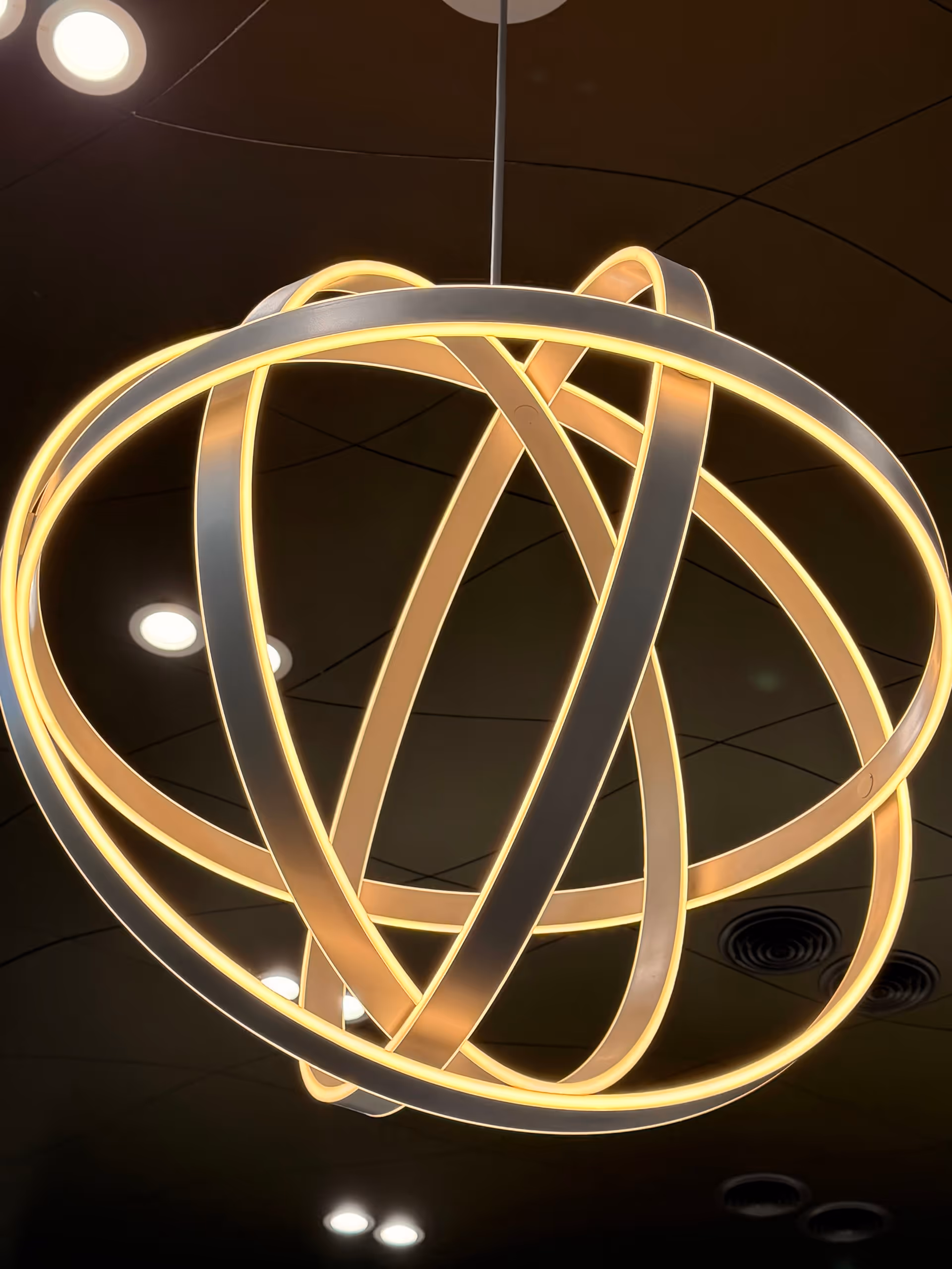 A modern chandelier with glowing intertwined loops hangs from a dark ceiling.