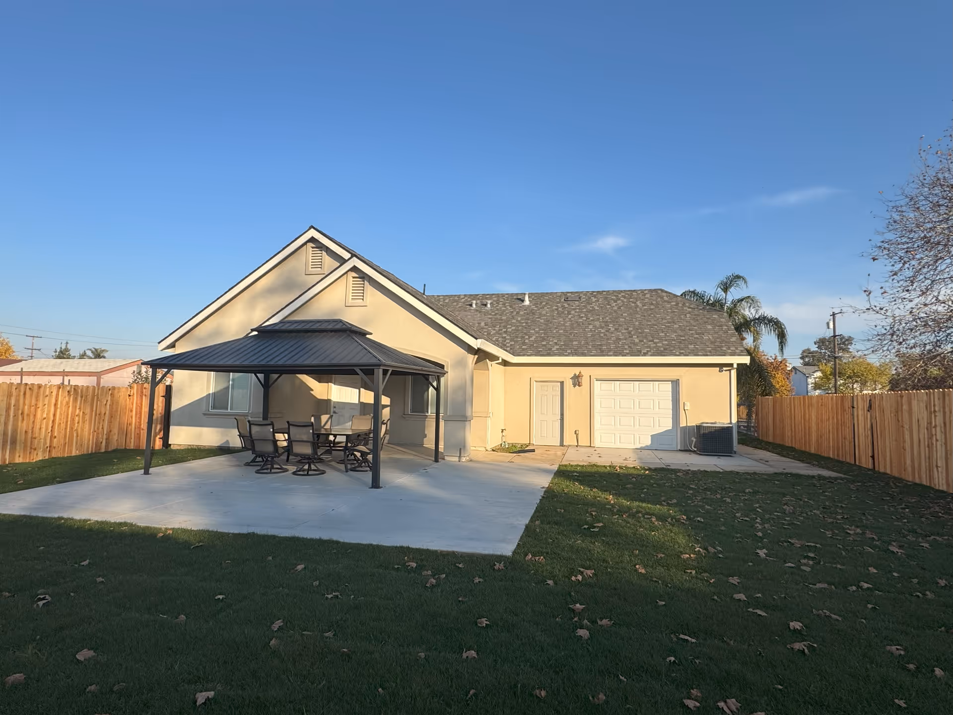 Single-story beige house with a covered patio and outdoor dining table in a fenced yard.