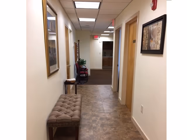 Long beige hallway in a senior facility with a bench, chairs, and framed art.