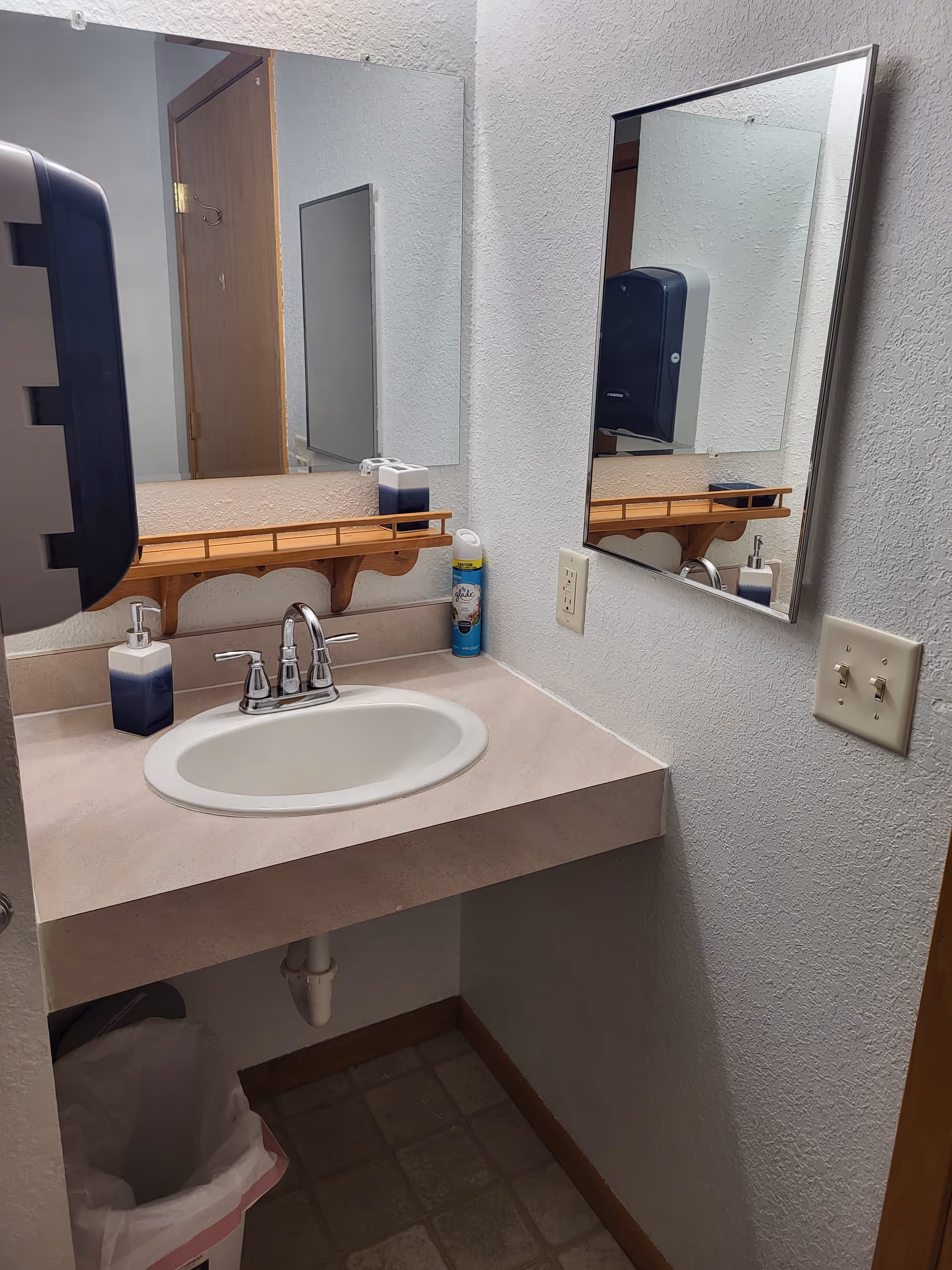Indoor bathroom sink area with mirrors, soap dispensers, and a trash bin.