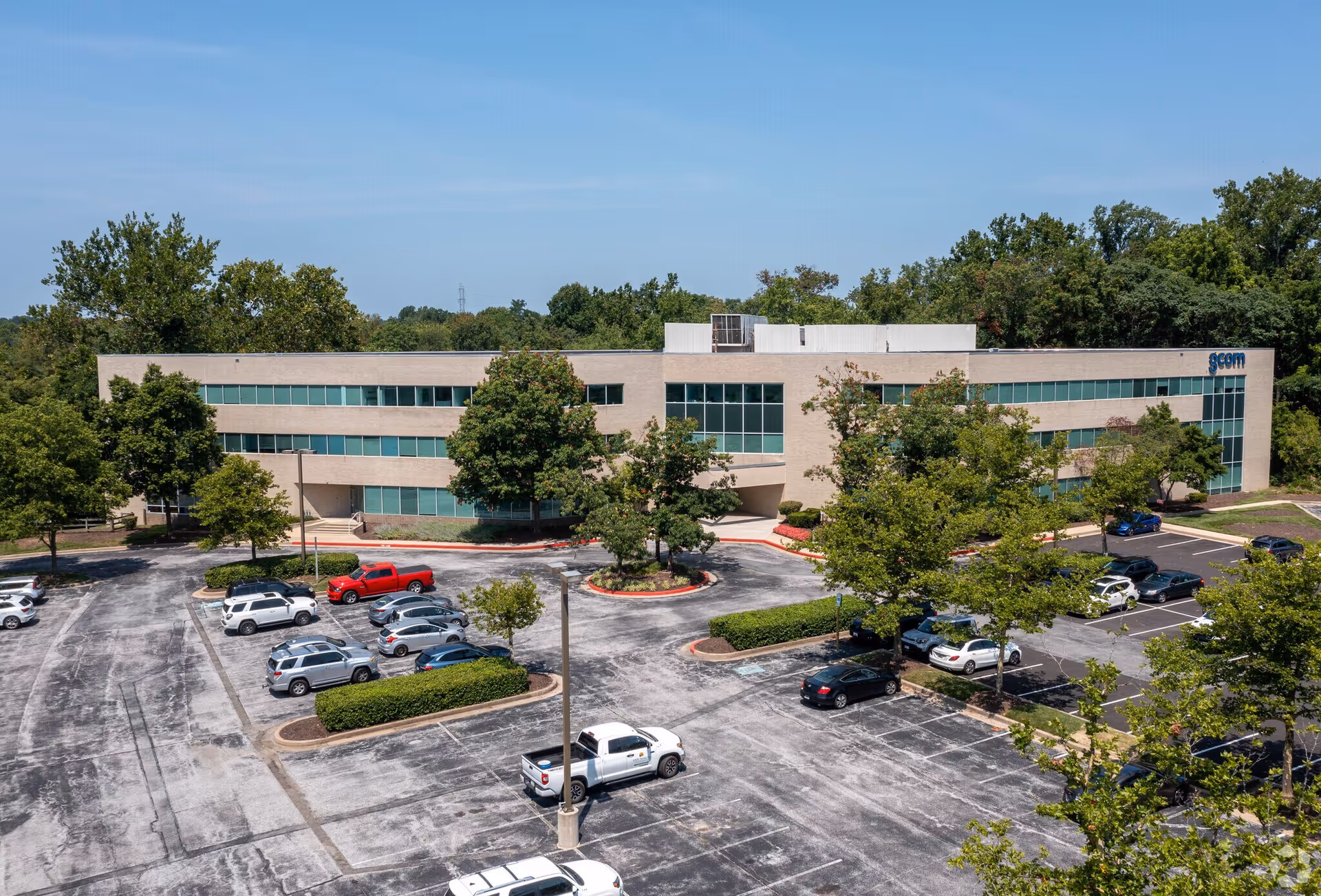 A modern two-story office building with glass windows and a surrounding parking lot.