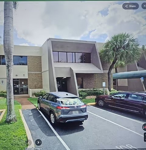 Exterior view of a senior care facility with parked cars and palm trees.