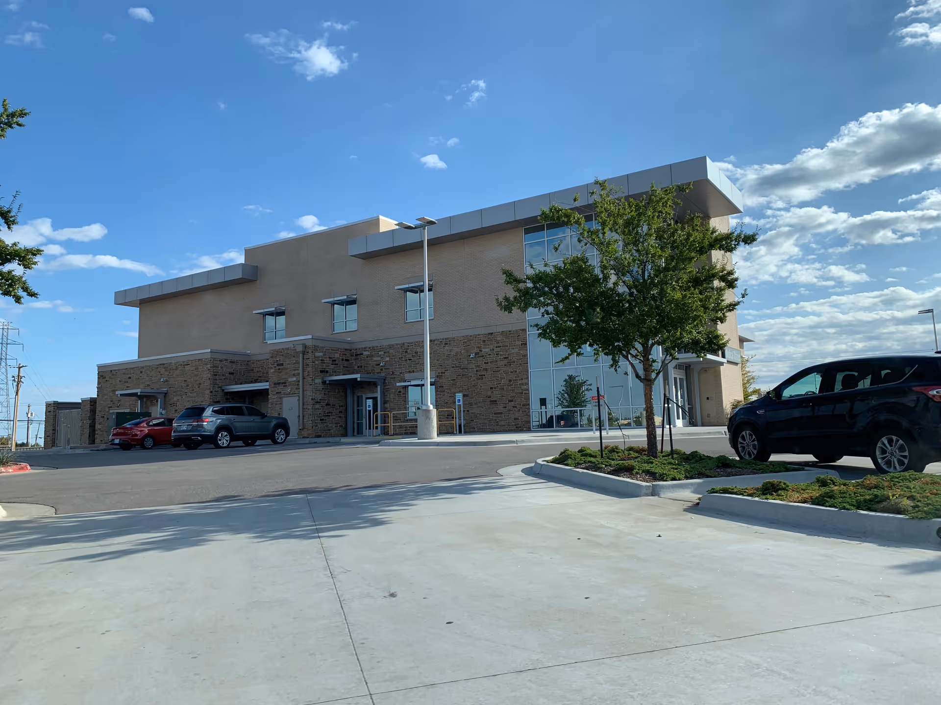 Exterior view of a modern hospital building with brick, glass facade and parked cars.