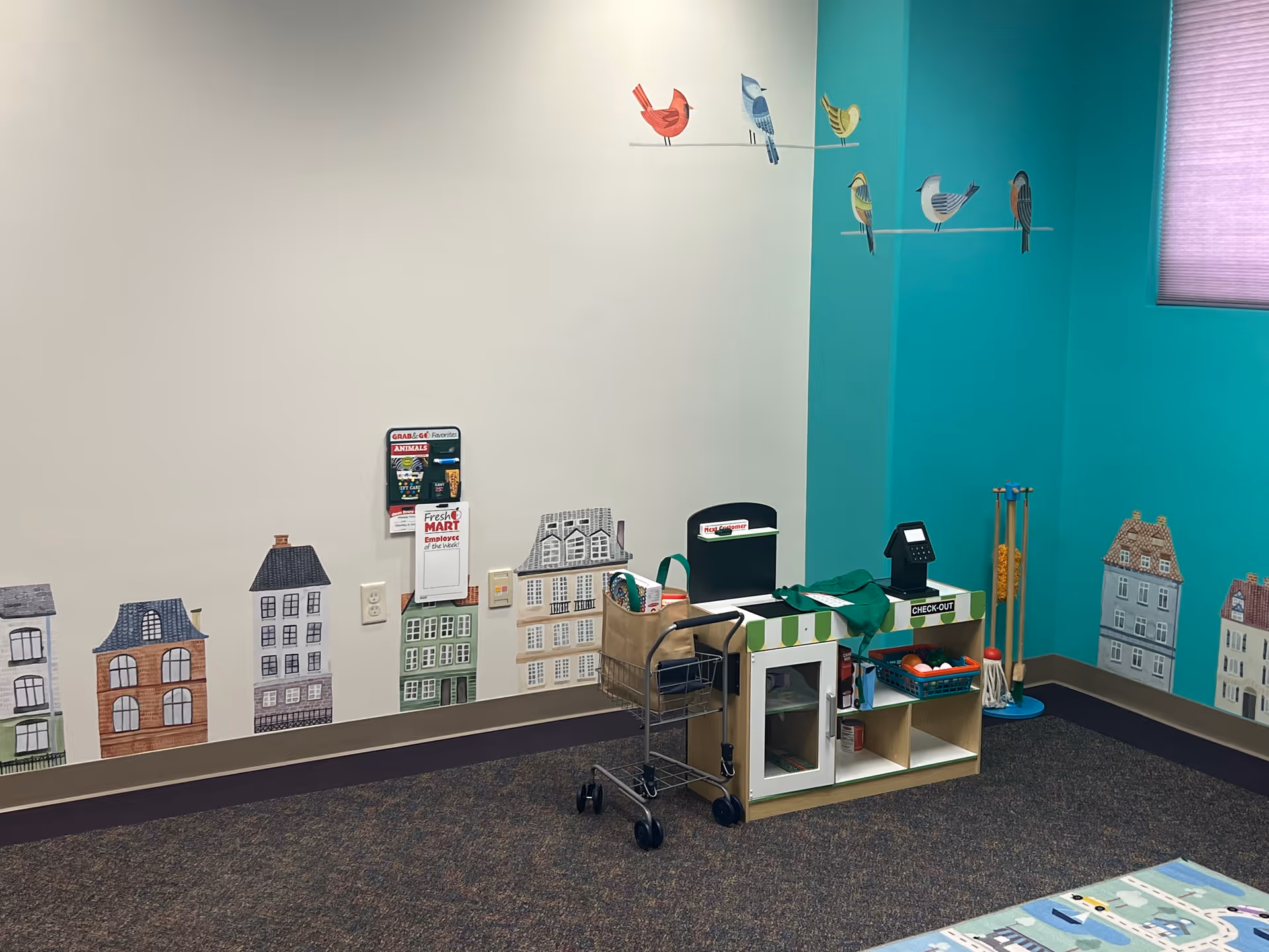 Colorful therapy play area with toy town walls, checkout station, and teal accent wall.