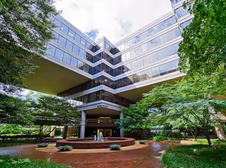 Exterior view of a glass-fronted senior living building with a brick courtyard and trees.