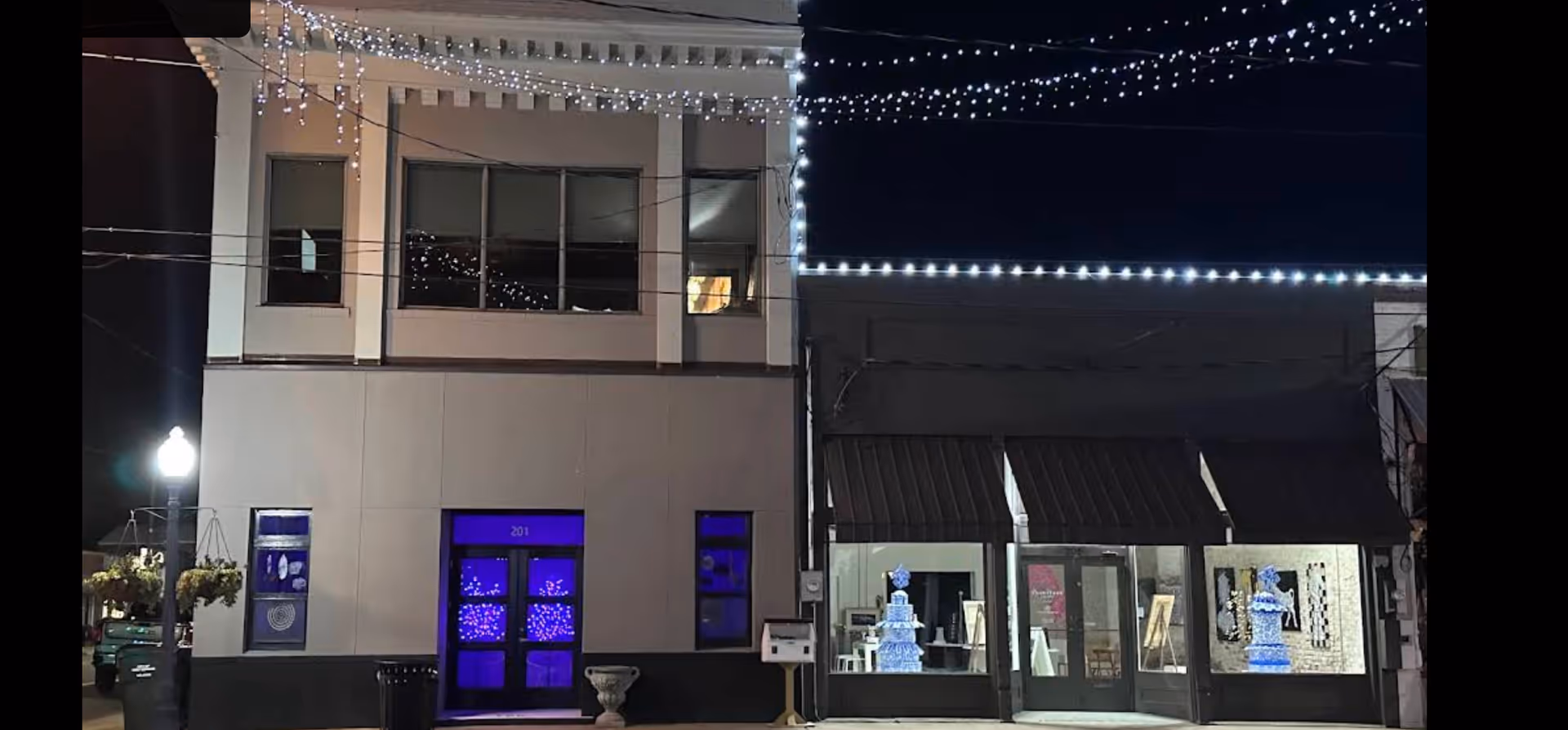Night exterior of a storefront row with string lights and illuminated windows.