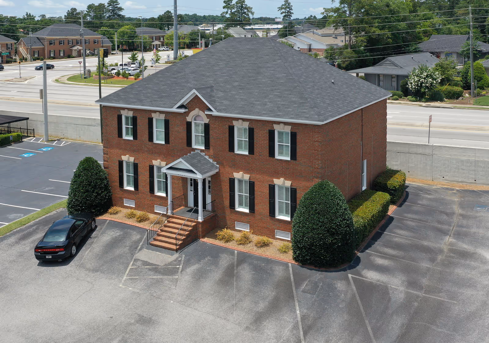A brick two-story building with stairs at the entrance, black shutters, and surrounding parking.
