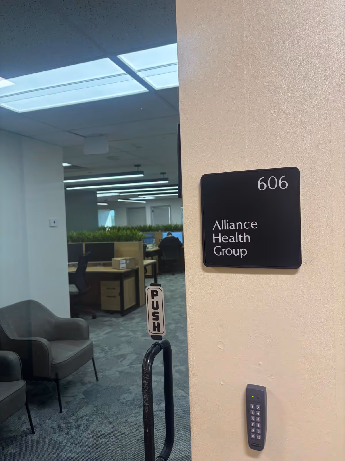 Office interior with desks, chairs, and a wall sign reading Alliance Health Group.