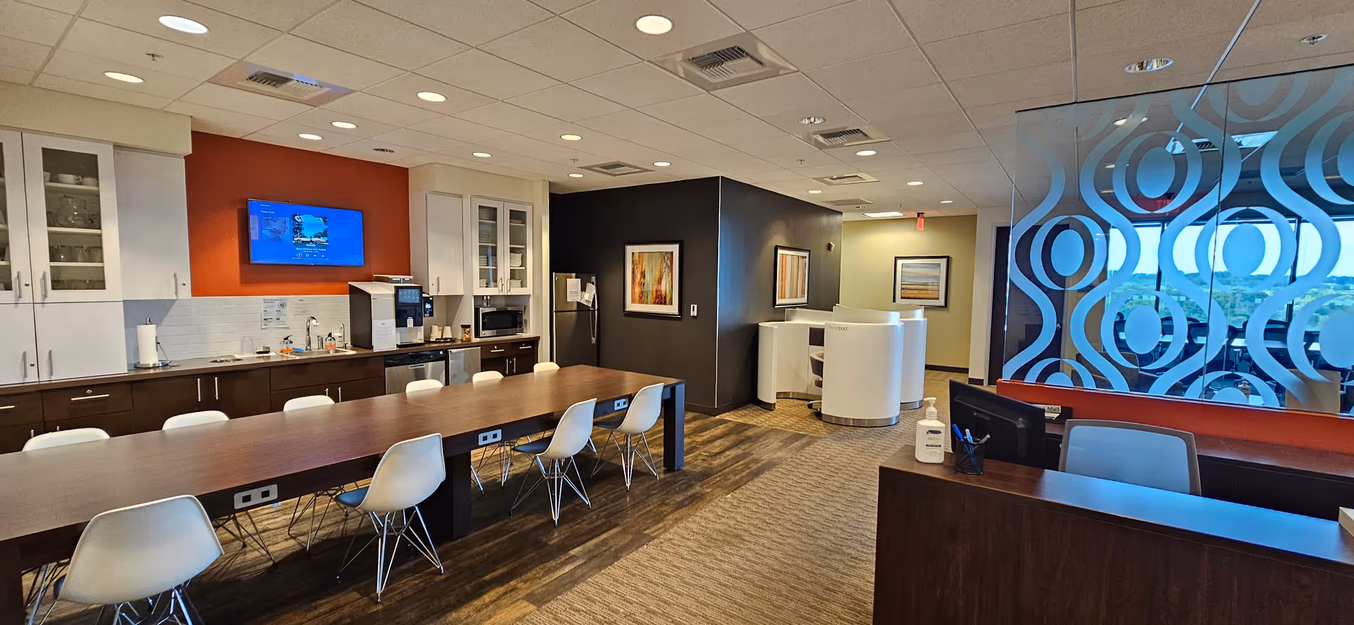 A modern senior living facility common area with a long dining table and kitchenette.