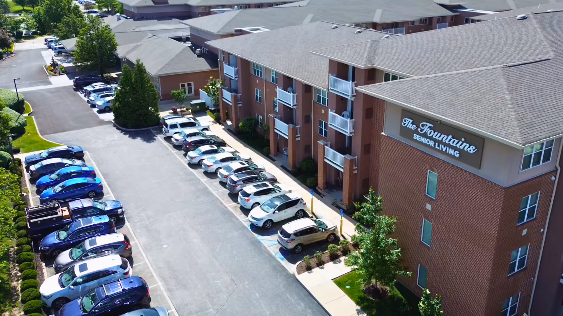 Aerial view of The Fountains Senior Living exterior with brick buildings and a long parking lot.