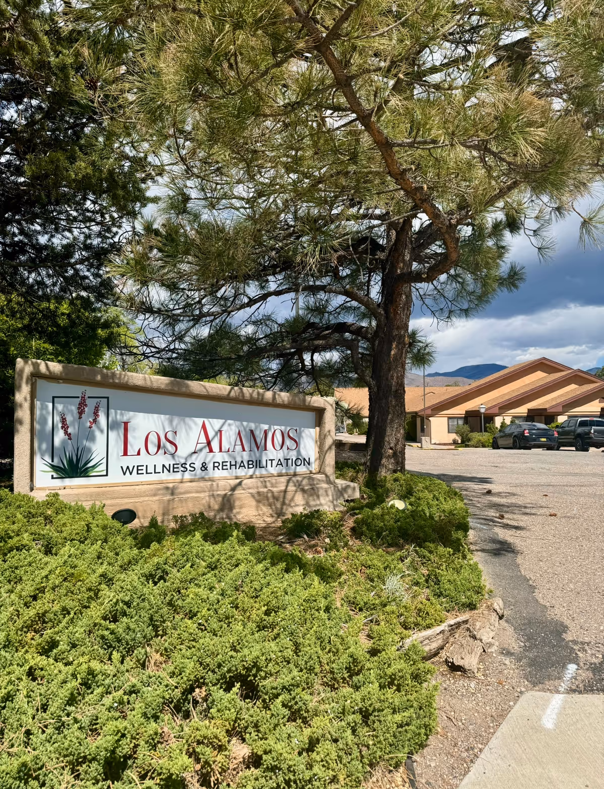 Stone sign reads Los Alamos Wellness & Rehabilitation in front of shrubs and a tree.