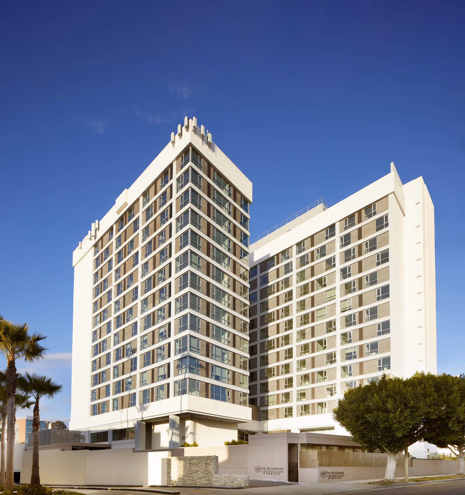 Front exterior view of a modern multi-story white residential building against a clear blue sky.