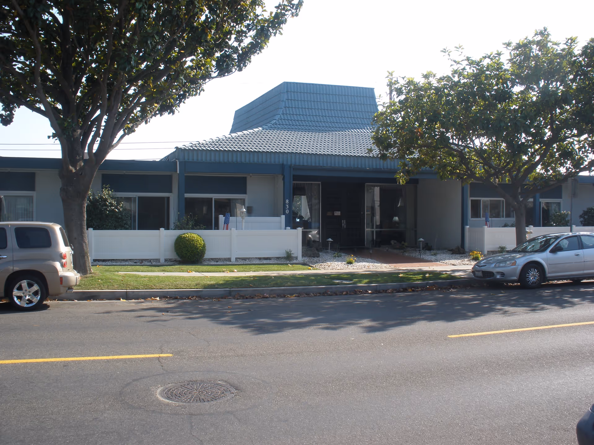Front view of Country Oaks Care Center with blue roof, white fencing, and trees.