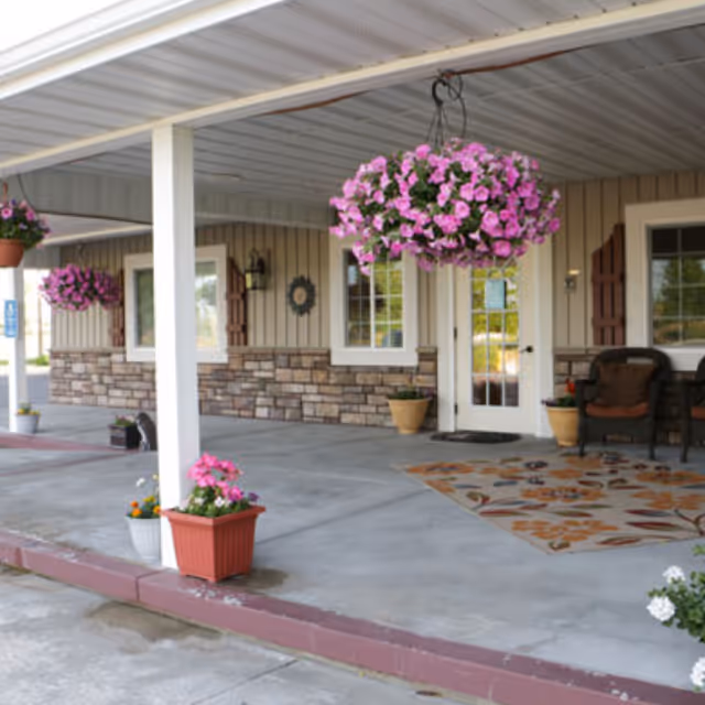 Front porch of a memory care facility with hanging flower baskets and potted plants.
