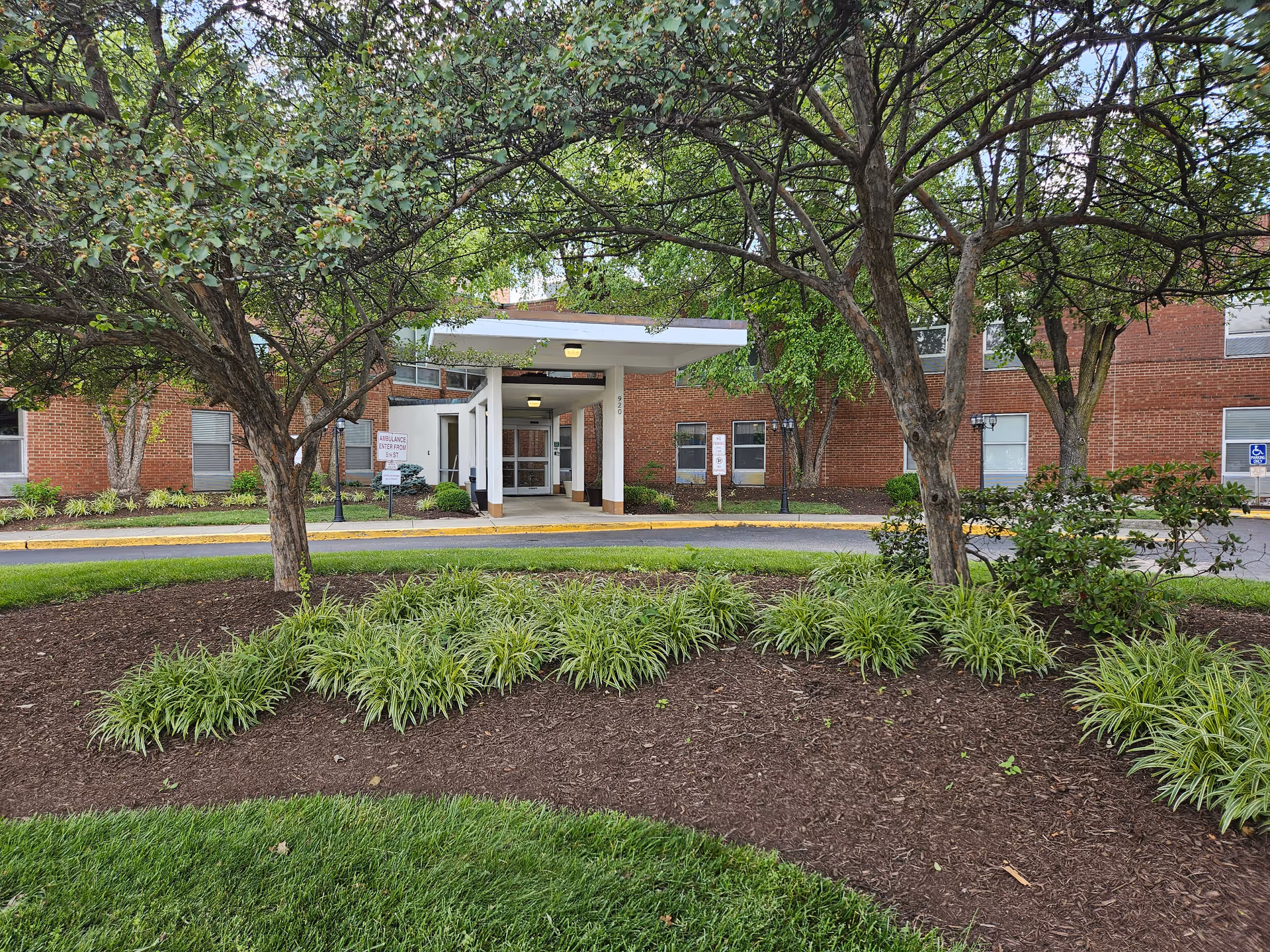 Exterior view of the facility entrance with trees, landscaping, and brick building.