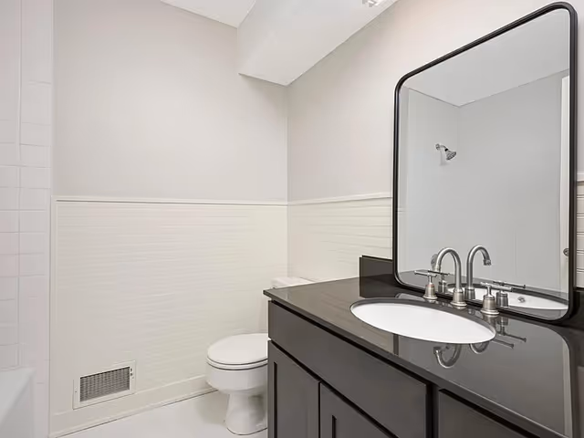 Modern bathroom with sink, vanity, mirror, and toilet.