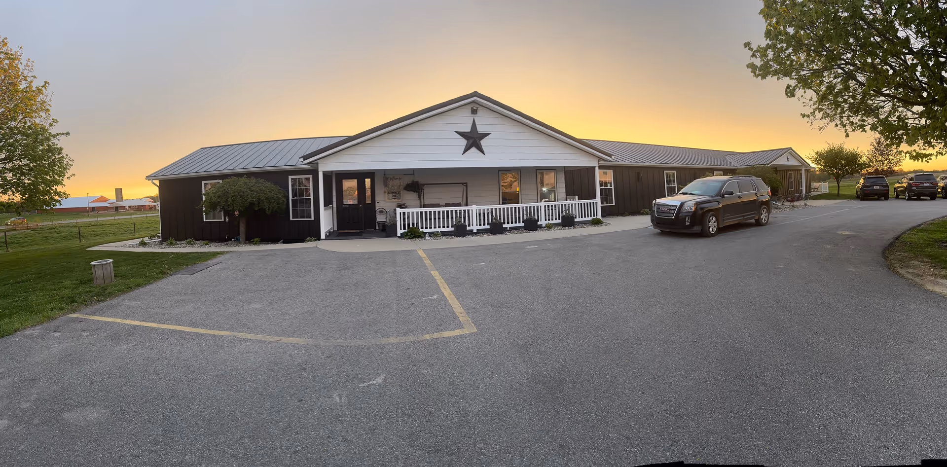 Sunset over SJ Flower House exterior, a dark building with star, white porch railing, and cars.