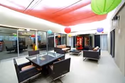 Indoor senior living facility lounge with wicker seating, a dining table, and colorful ceiling lanterns.