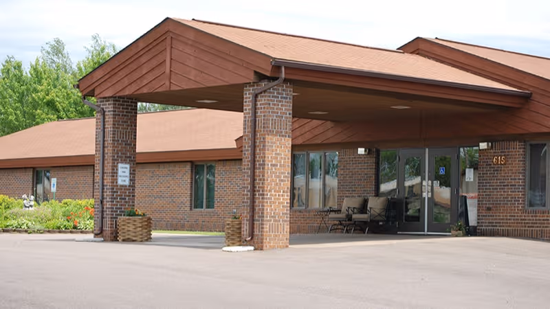 Brick senior living facility entrance with a covered portico and outdoor seating.