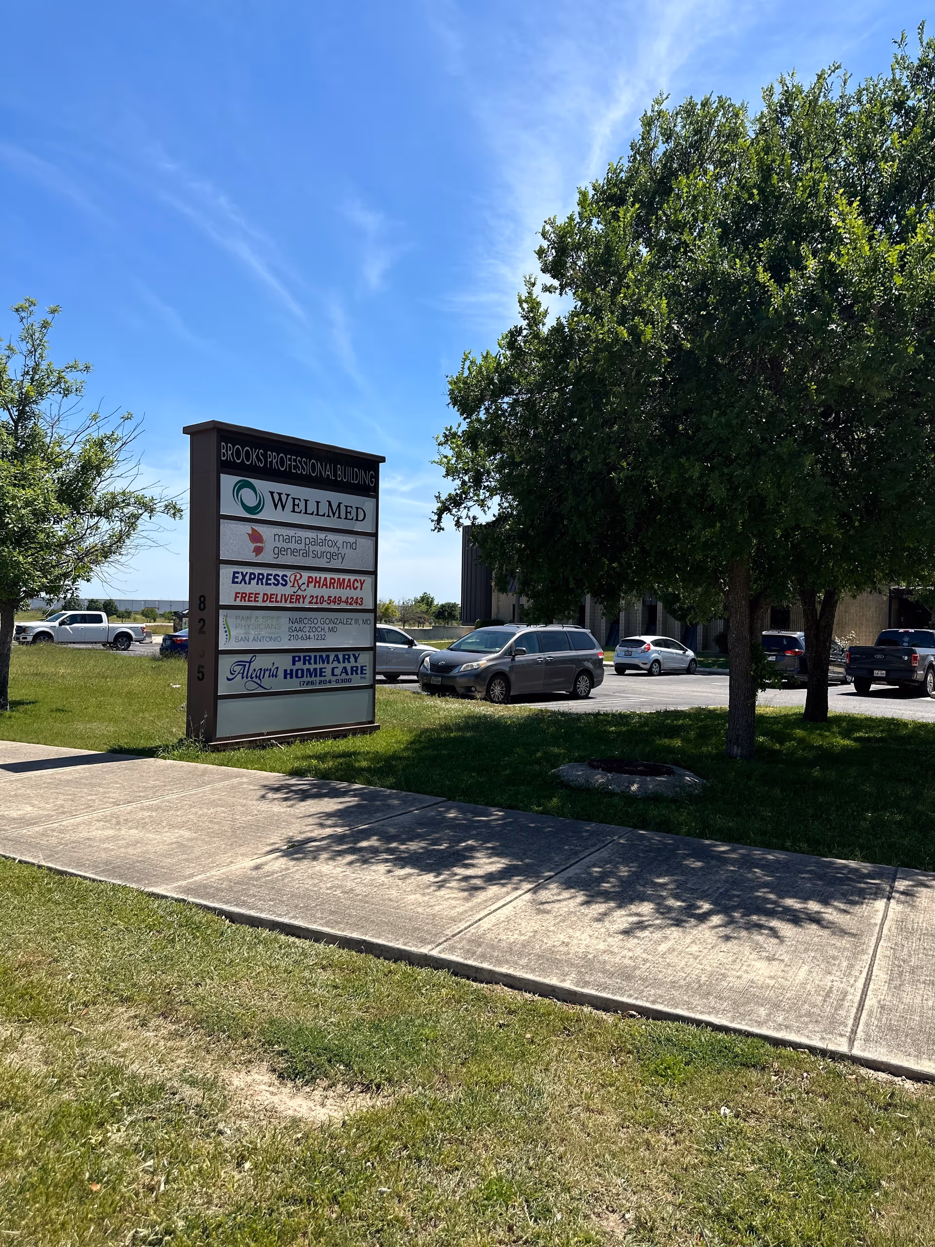 Outdoor view of a sign for Alegria Primary Home Care with trees and parked cars.