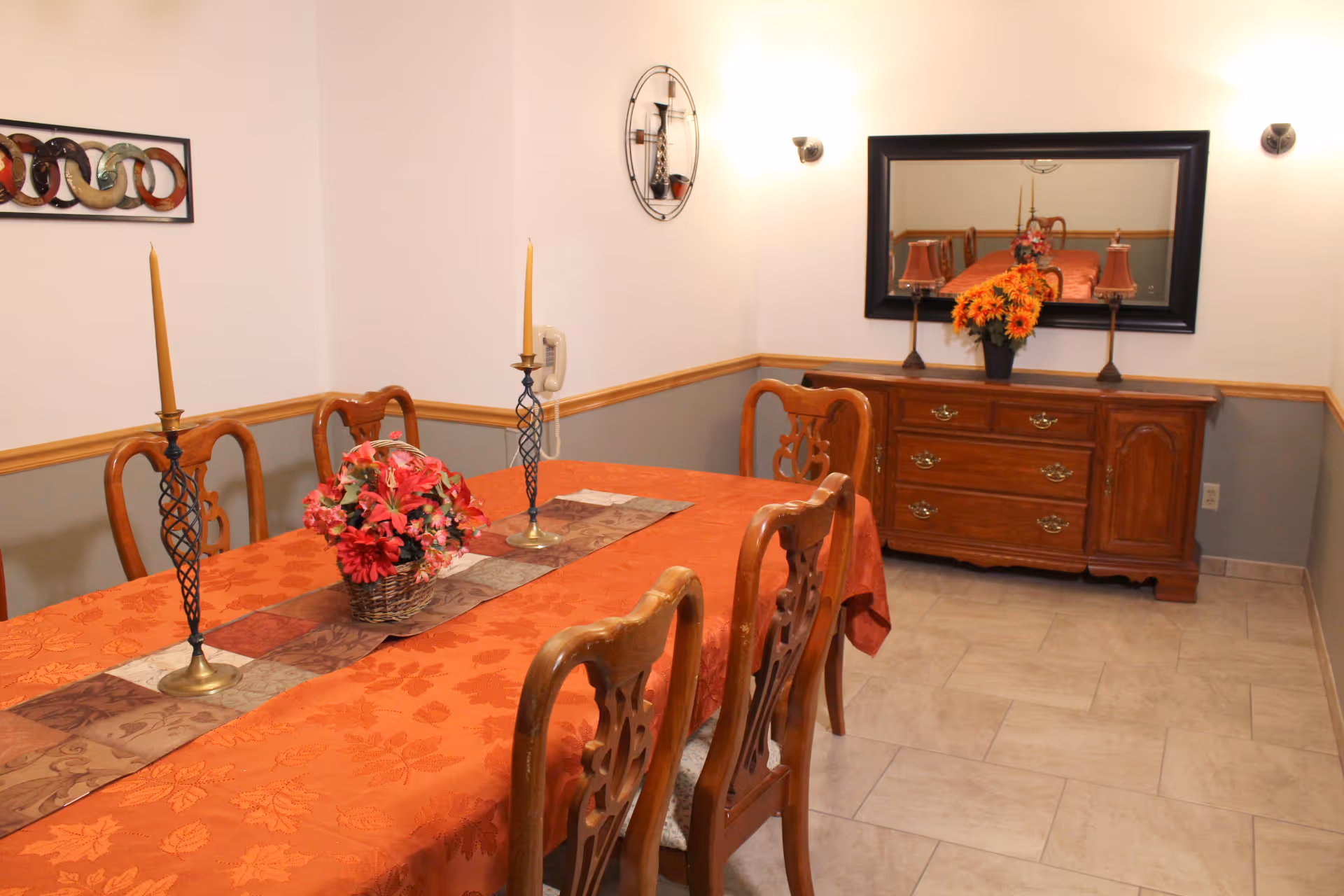 A dining room with an orange tablecloth, candles, and wooden chairs.