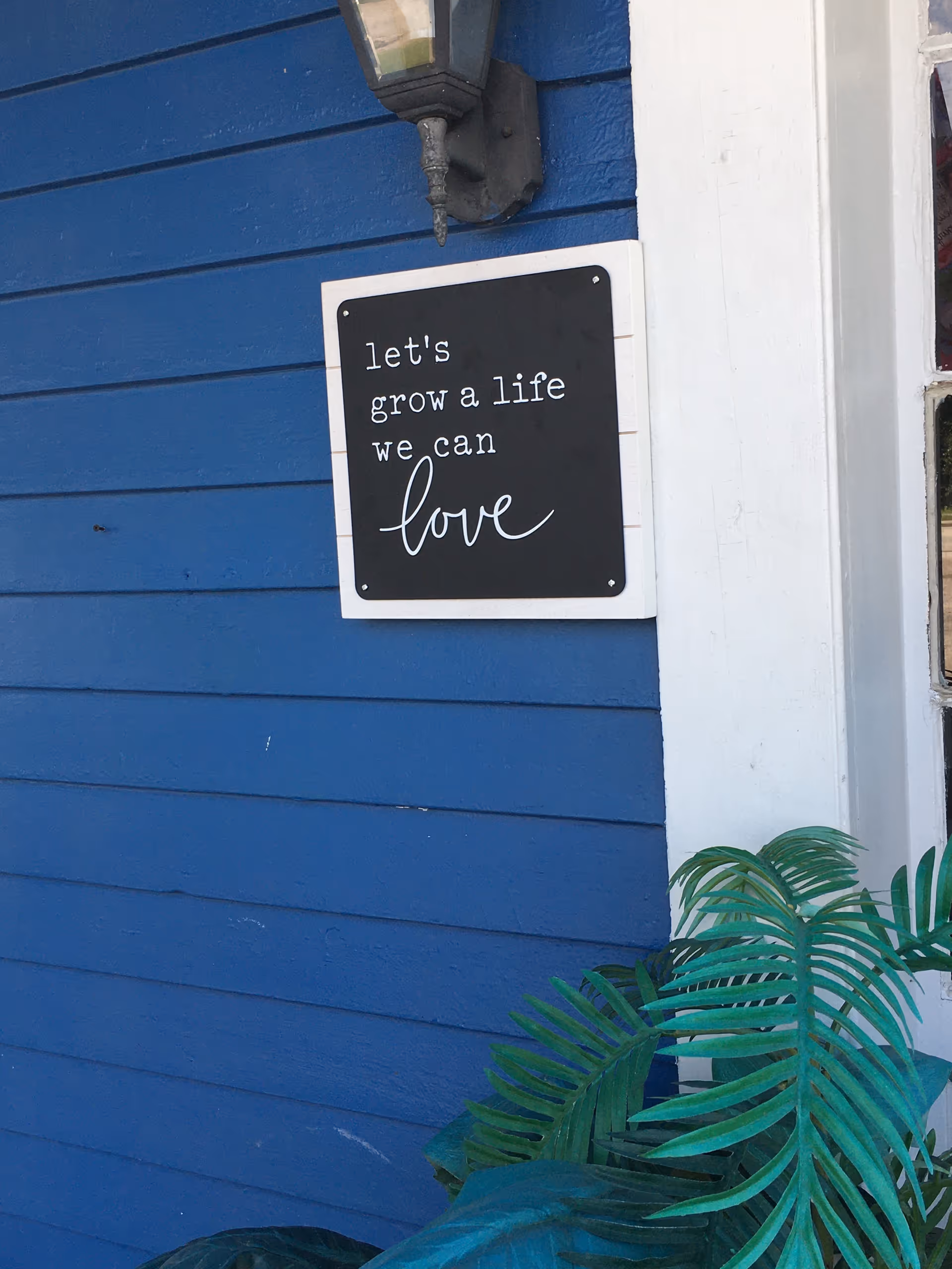 Blue exterior wall with a sign reading 'let's grow a life we can love' and plants.