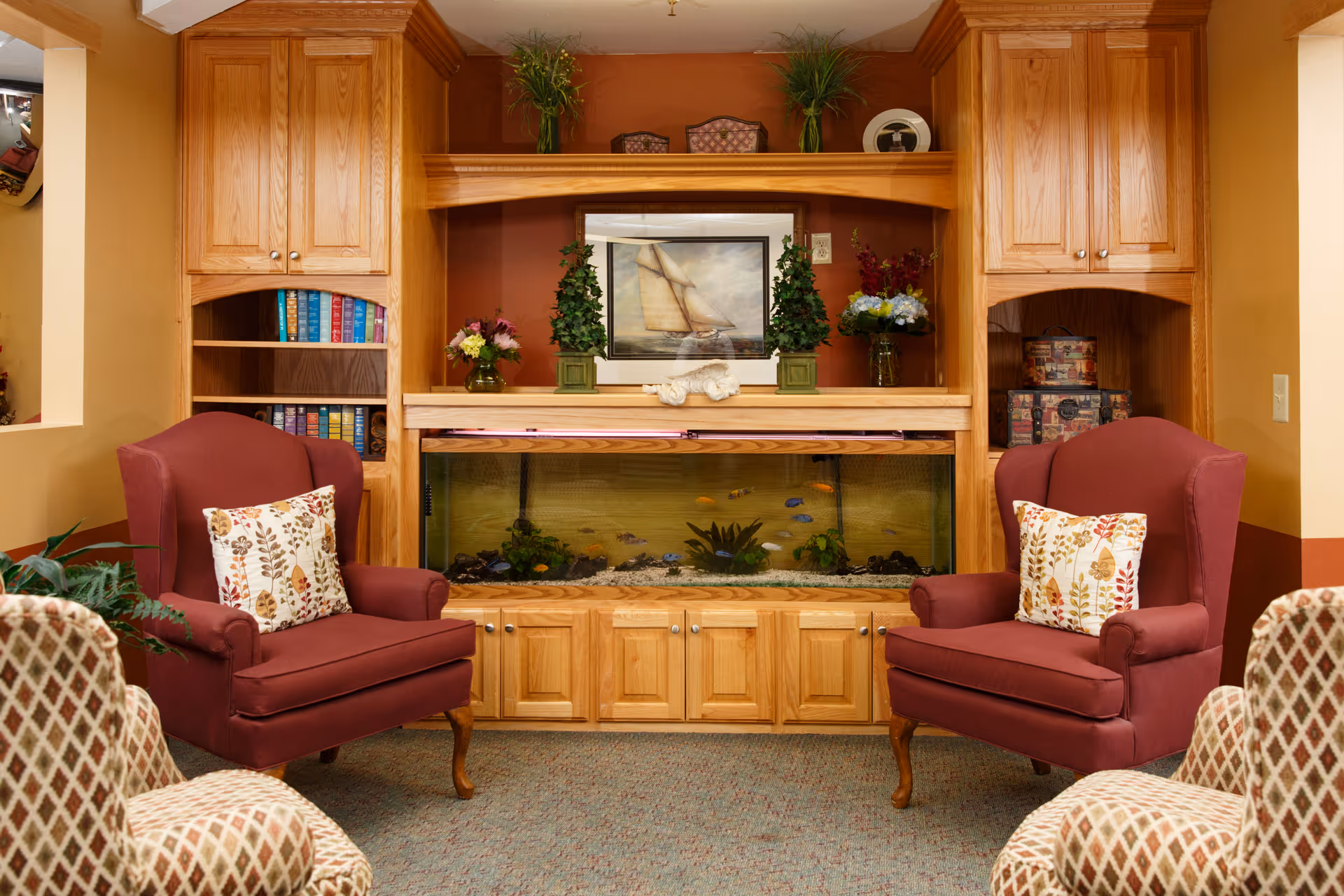 Cozy seating area with two burgundy armchairs facing a built-in wooden cabinet featuring an aquarium and decorative items.