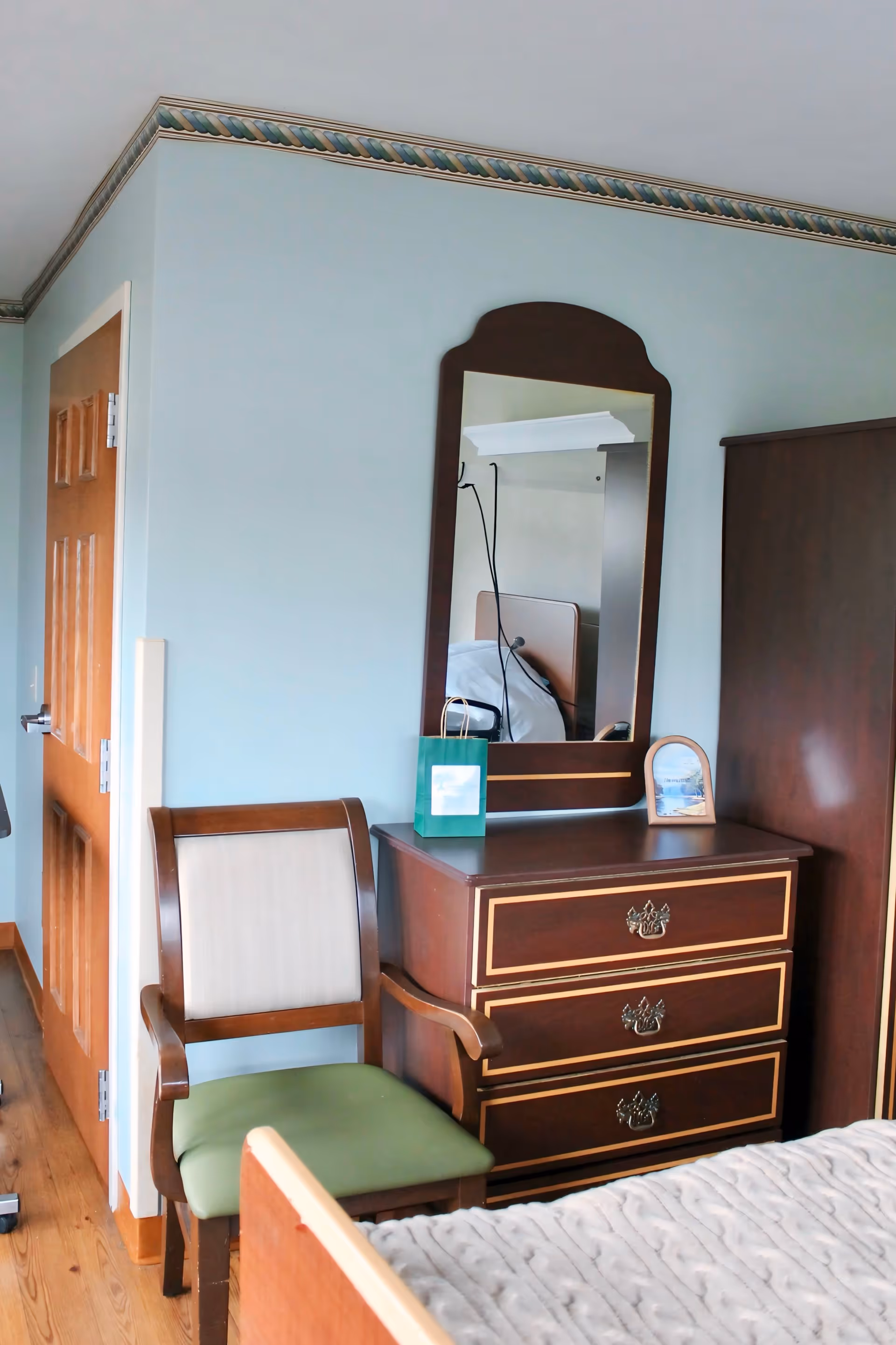 A furnished bedroom at Salmon Brook Rehabilitation and Nursing Center with a dresser, mirror, and chair.