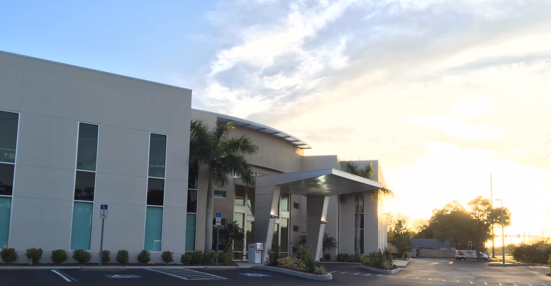Modern senior living facility exterior with covered entrance, parking, and palm trees.