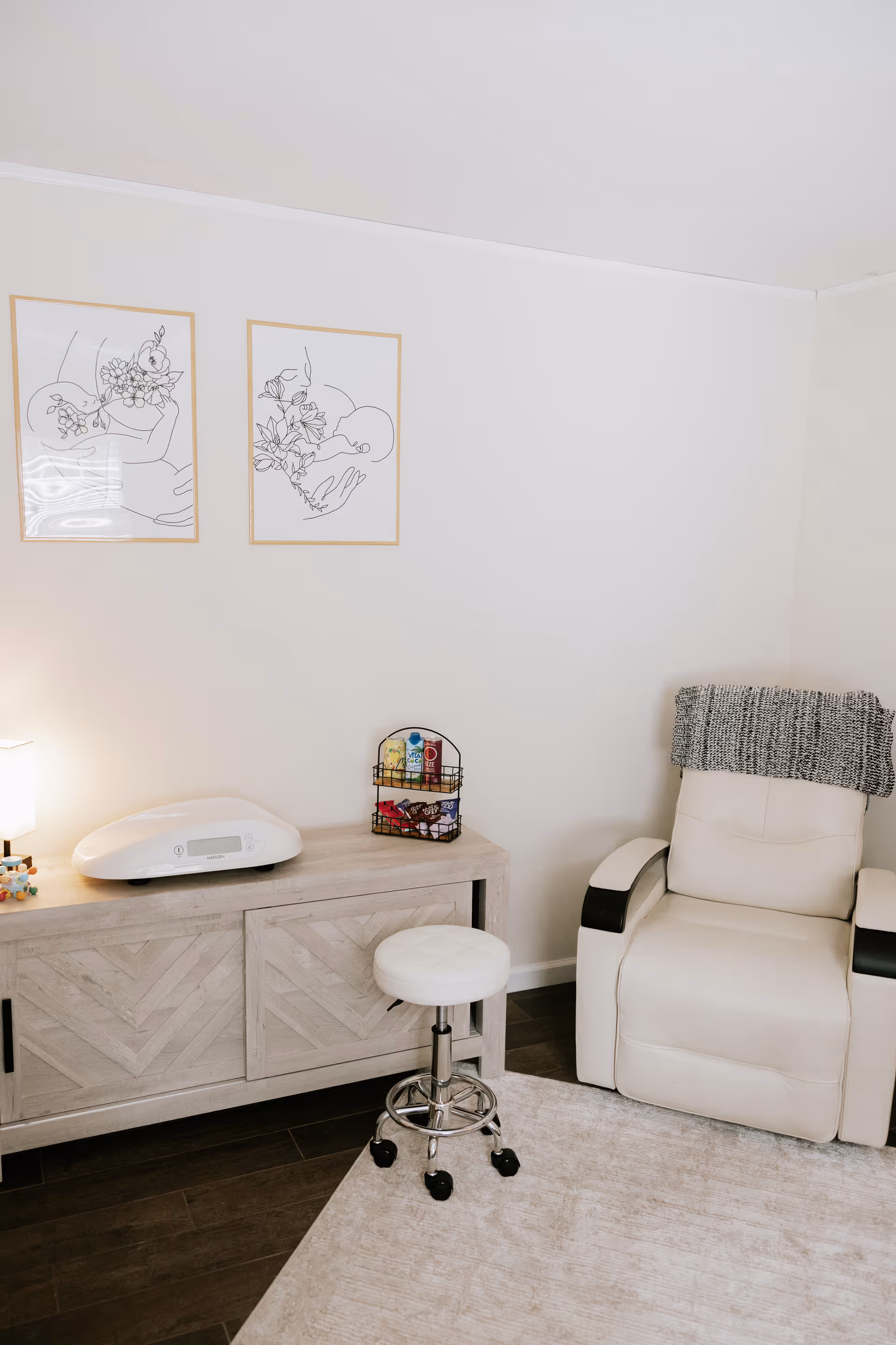 Light-filled interior room with a treatment chair, cabinet, stool, and wall art.