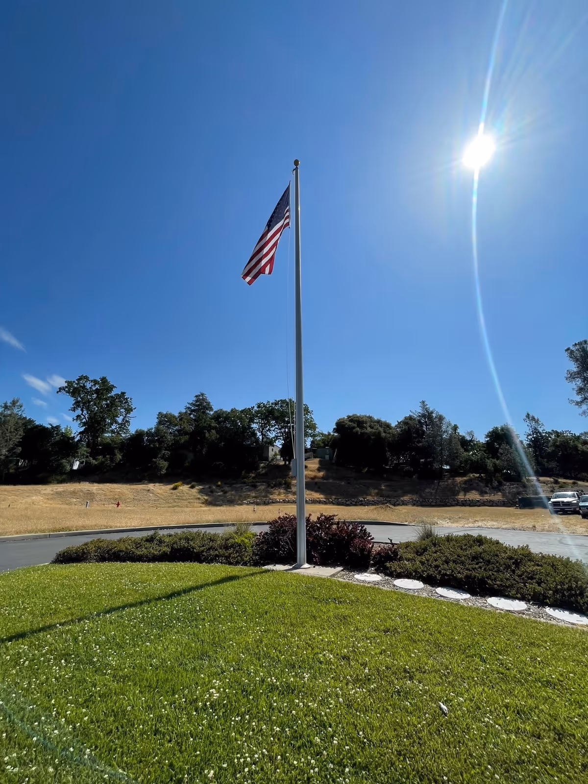 American flag on a tall pole in a well-kept grassy roundabout outdoors.