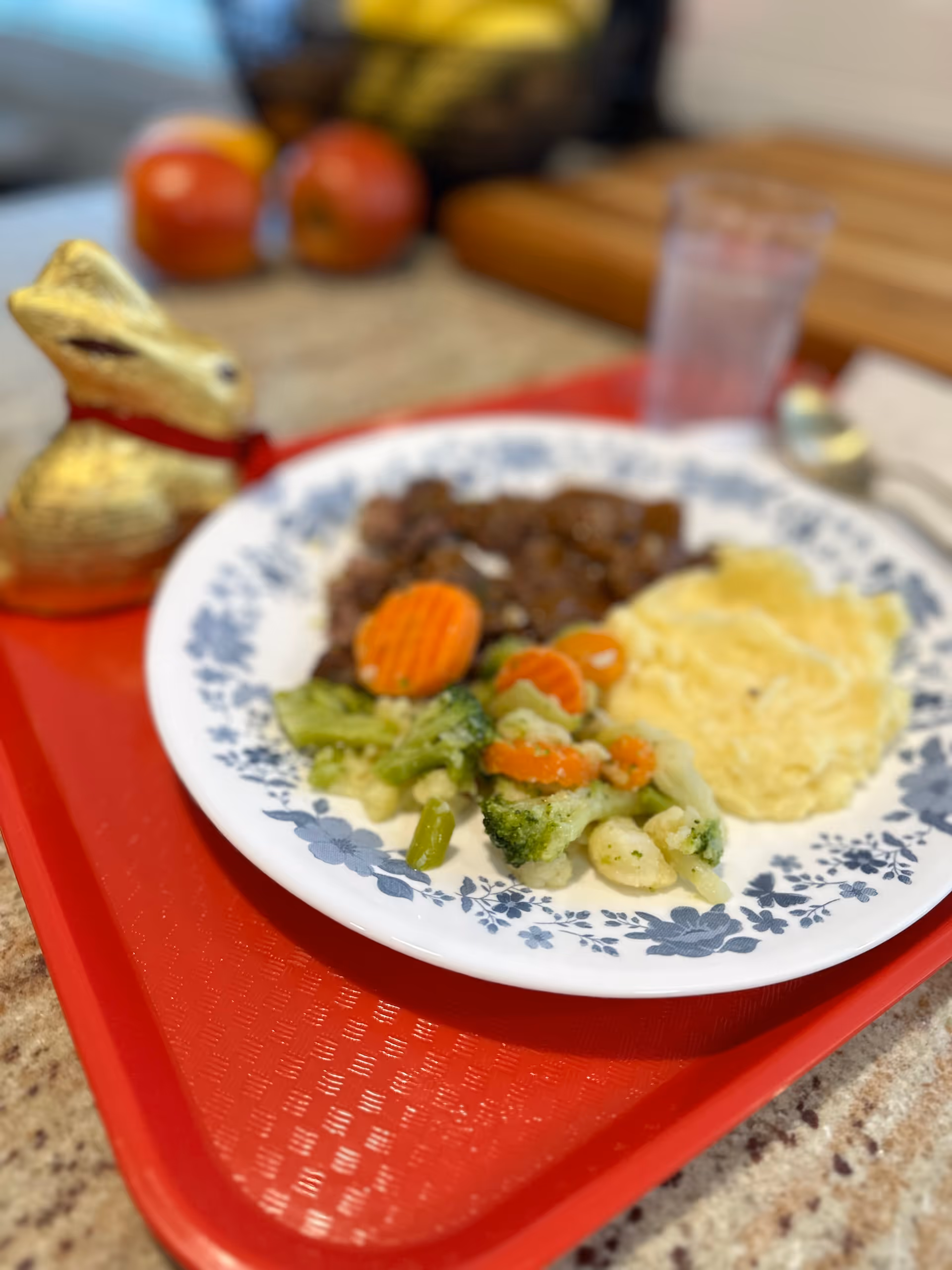 Plate of vegetables, mashed potatoes, and meat on a red serving tray in a dining setting
