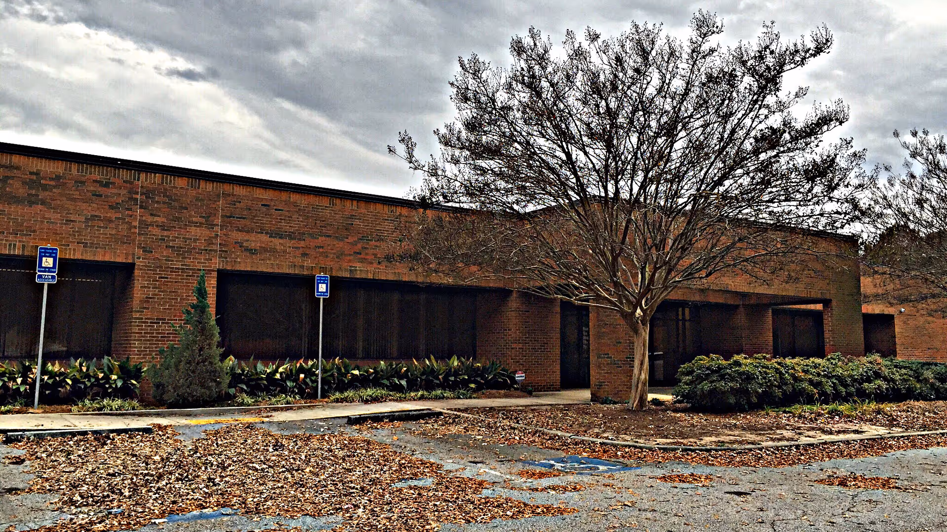 Brick senior living facility exterior with a leafless tree, shrubs, and handicapped parking in foreground.