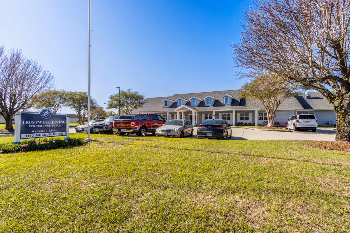Trustwell Living at Terrebonne Place front entrance with parked cars and sign on the lawn.