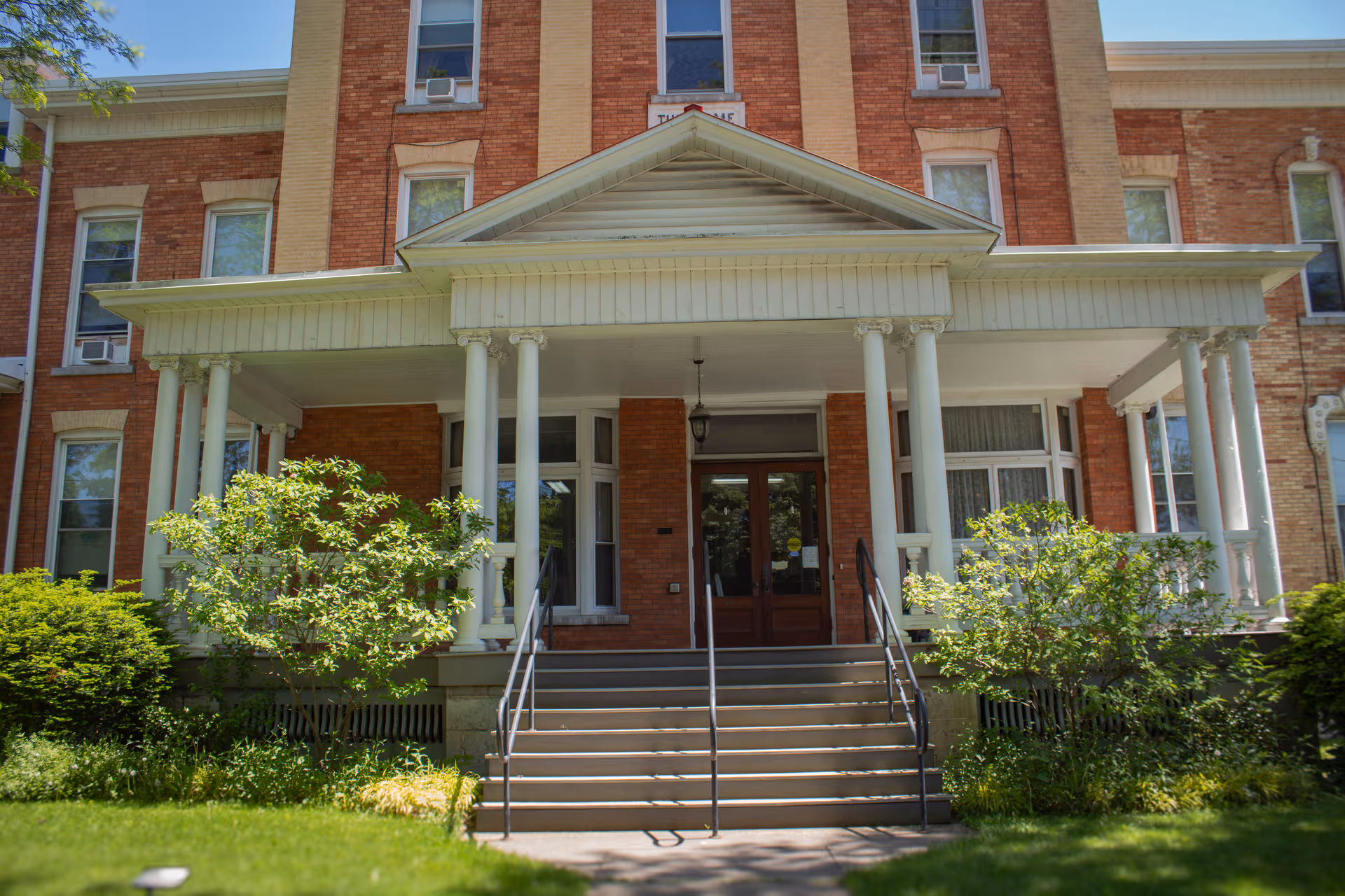 Brick senior living facility with columns, a covered entrance, and central staircase.